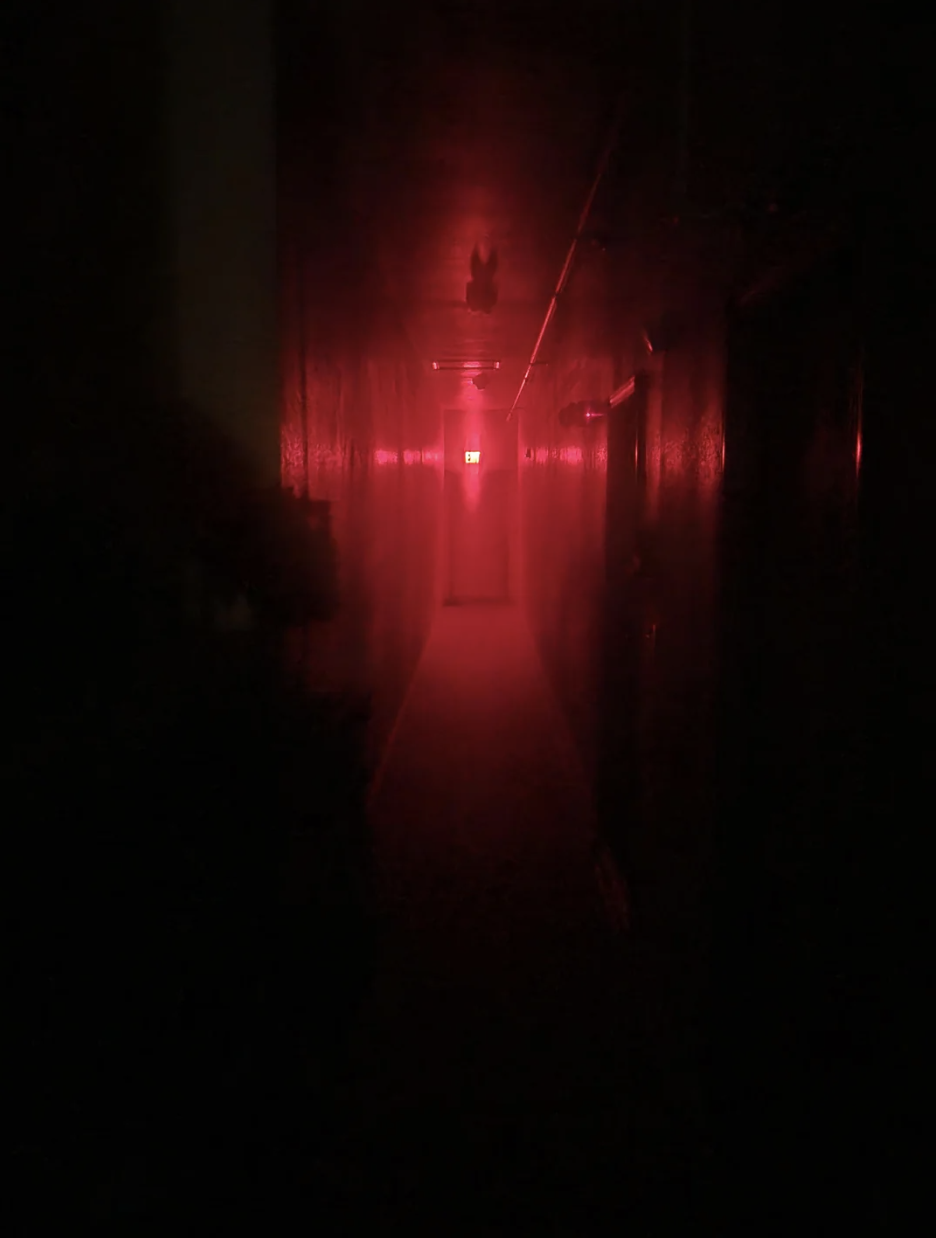 Dimly lit hallway with red lighting and an exit sign at the end