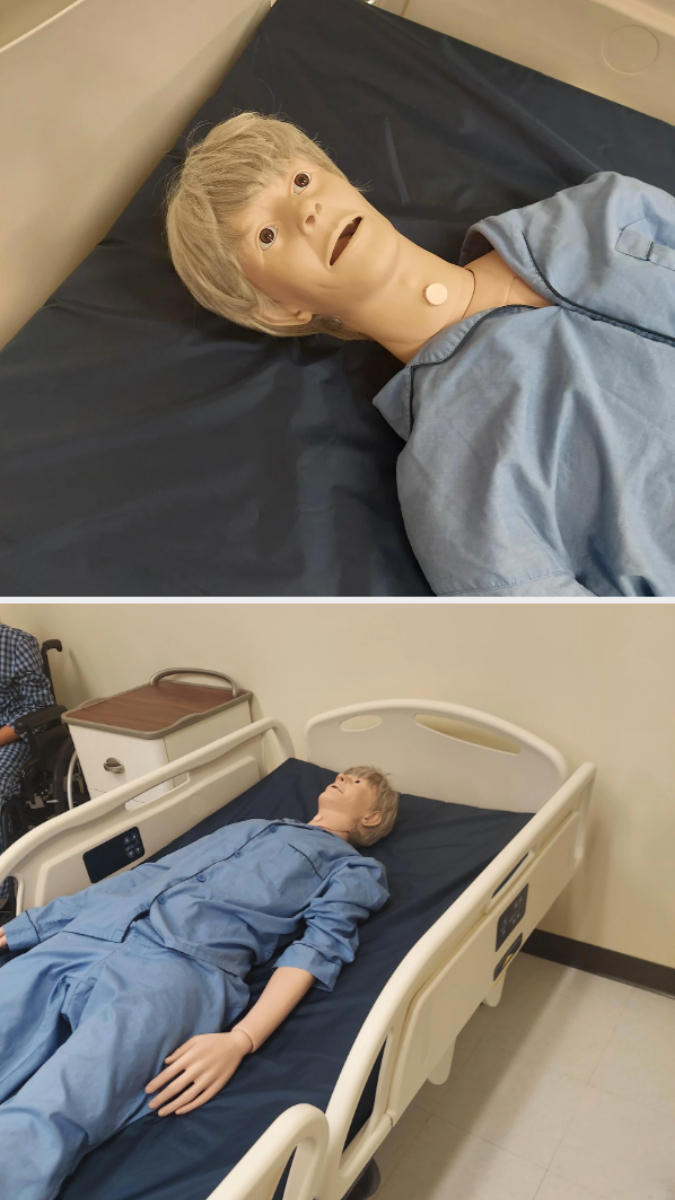 Medical training mannequin lying in a hospital bed wearing a blue gown