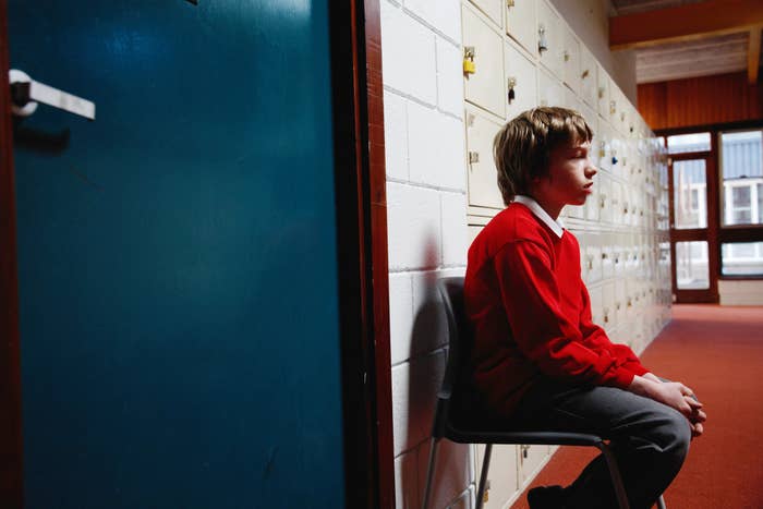 Child sitting beside lockers, appearing thoughtful
