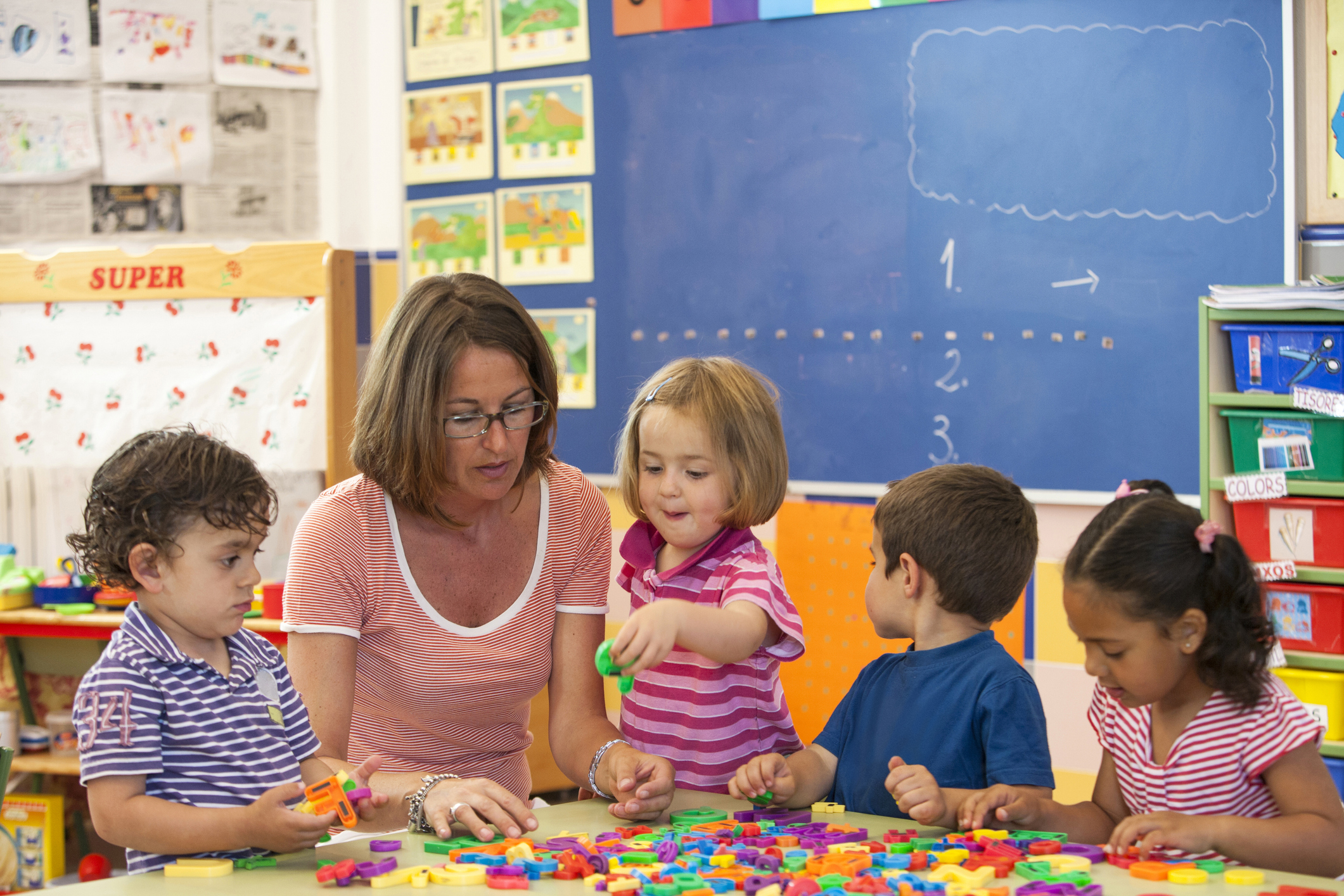Teacher and four children engaging with colorful building blocks on a table in a classroom
