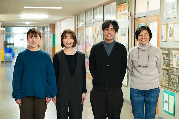 廊下に並んで立つ4人の人物。左から3人目の男性以外は女性。