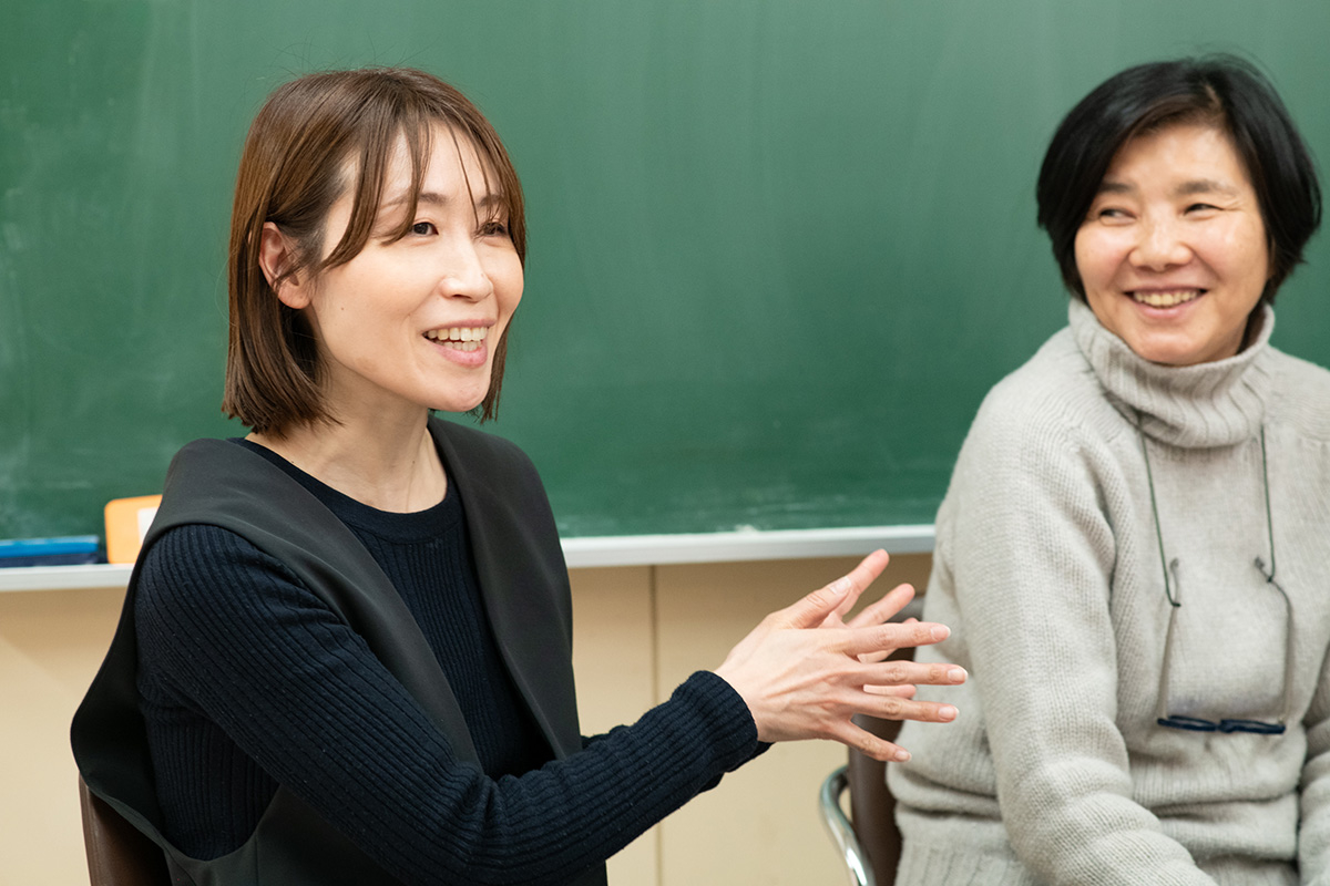 教室で笑顔の女性二人がおしゃべりしている。
