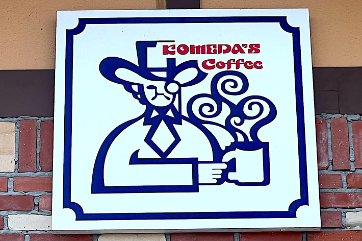 Sign for “SOMEDAY’S Coffee” featuring a stylized figure holding a coffee mug with steam rising from it