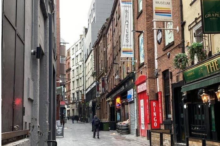 A person walking through a narrow, historic city street lined with shops and a Beatles museum sign