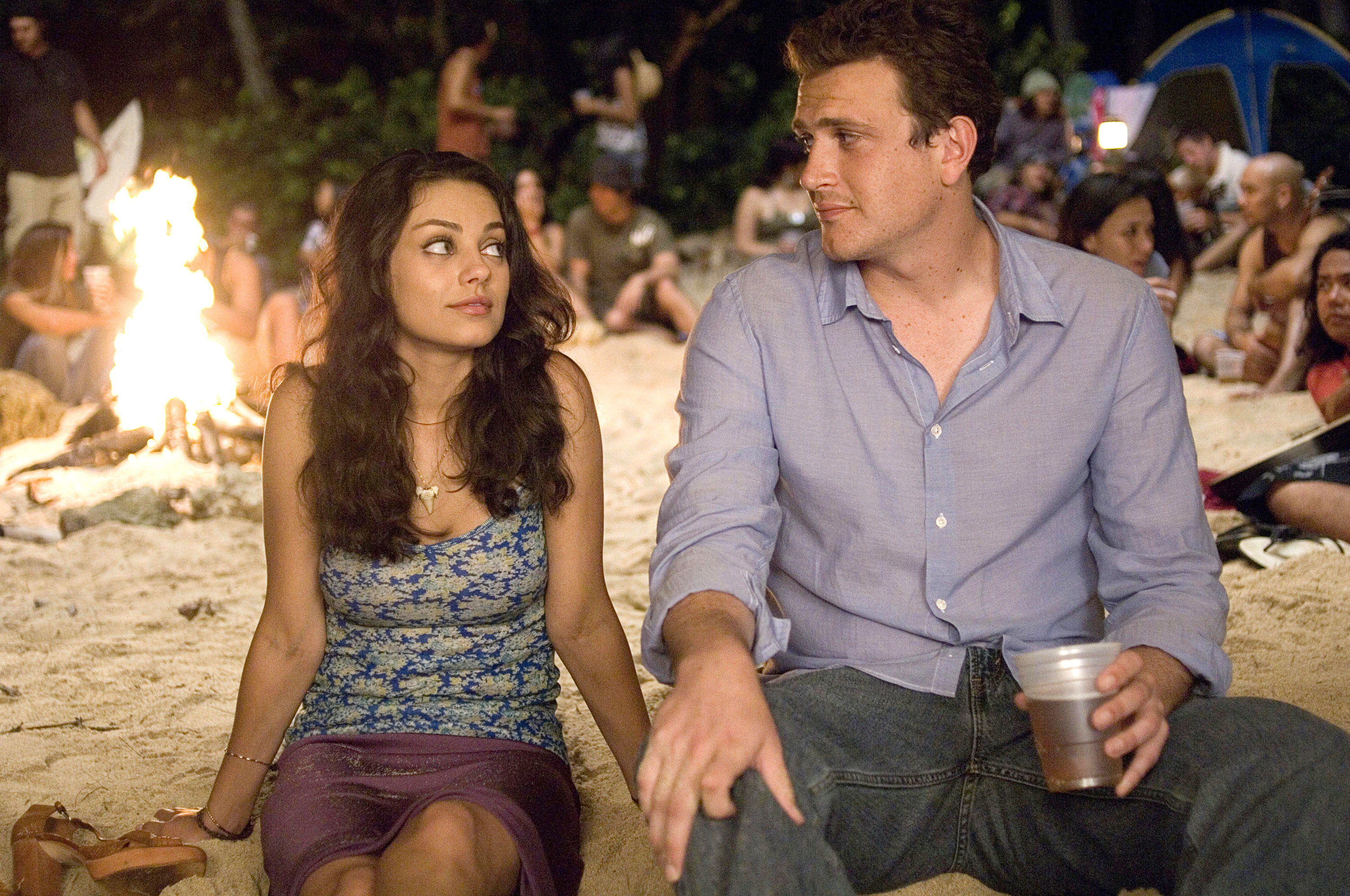 Mila Kunis and Jason Segel sitting by a campfire on a beach in a scene from a movie