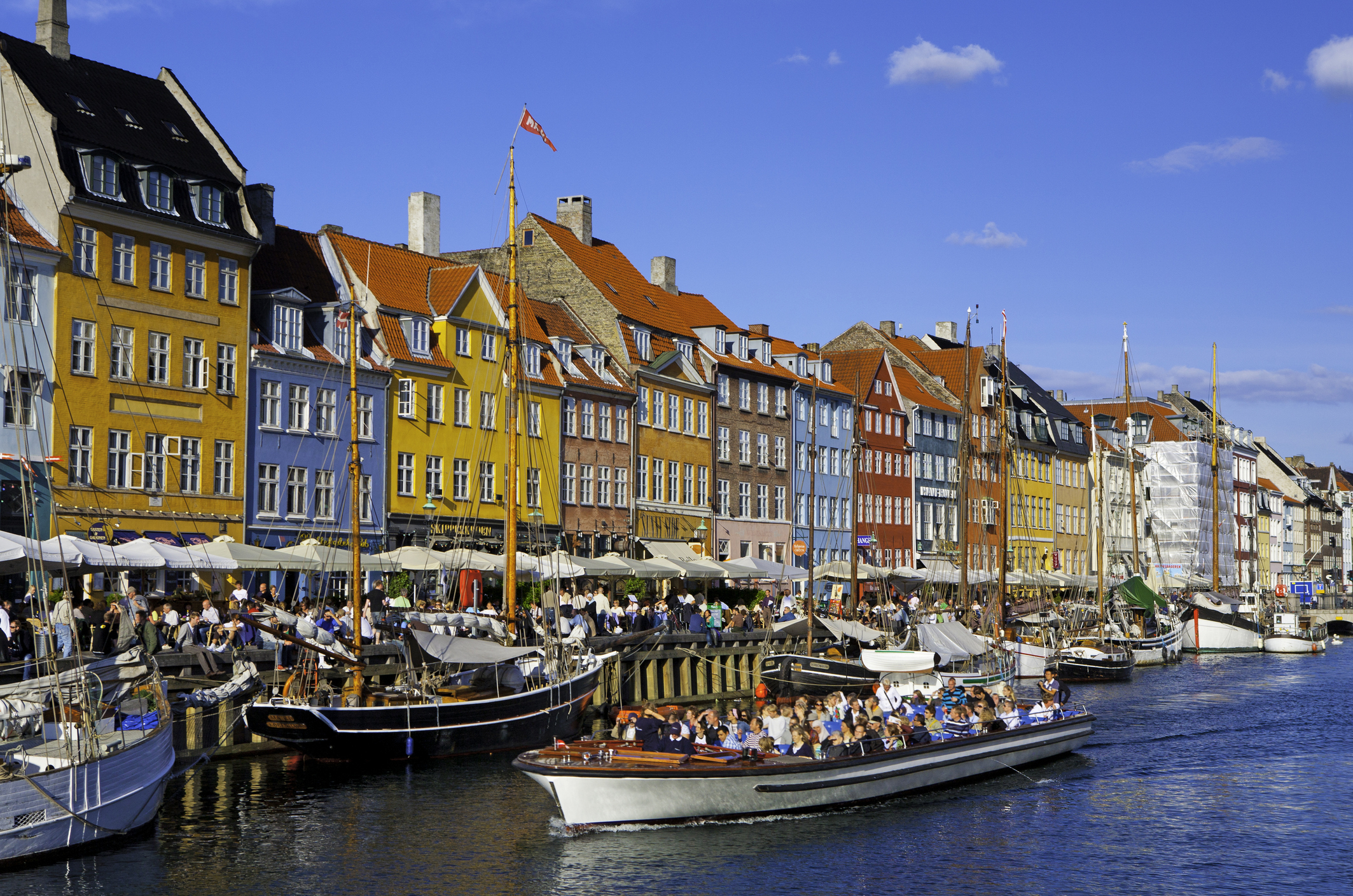 Scenic view of Nyhavn canal with boats and lined with buildings, people dining by the waterfront