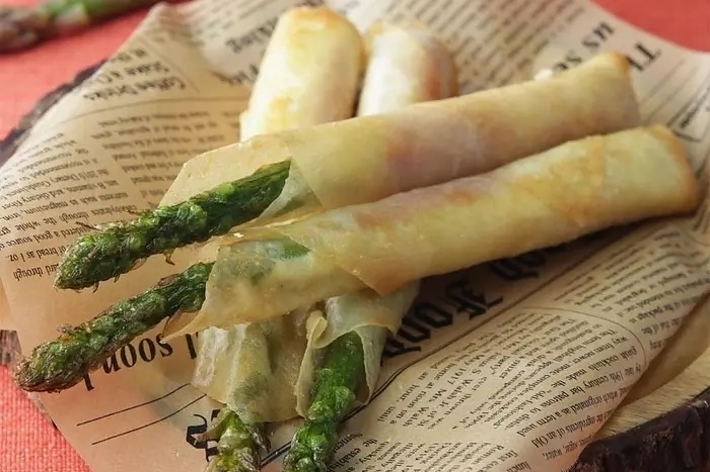 アスパラガスが巻かれた春巻きが新聞の上に置かれている。