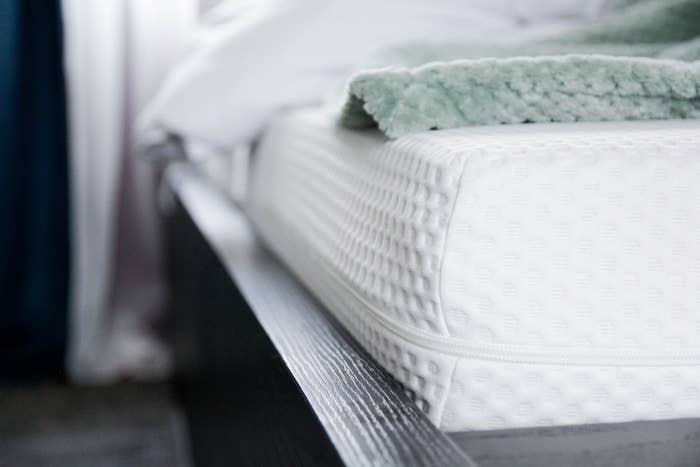 Close-up of a mattress with textured fabric, a white sheet, and a soft green blanket on top