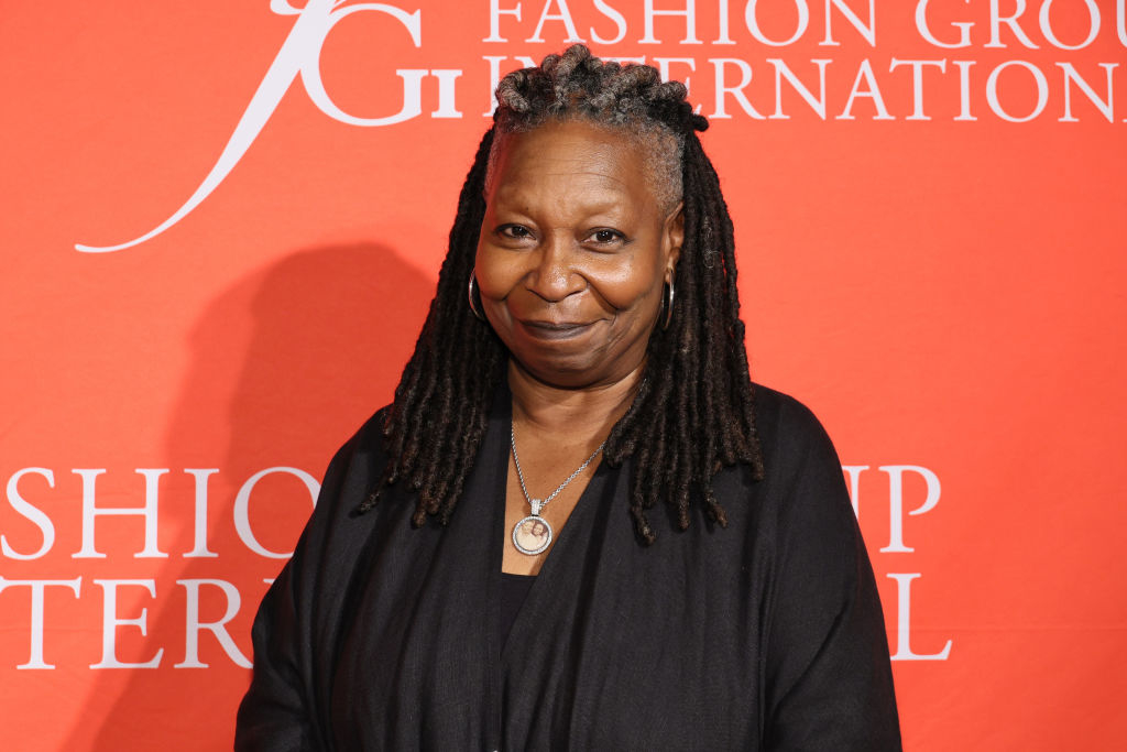 Whoopi Goldberg on the red carpet wearing a black outfit with a round silver pendant