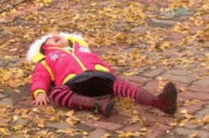 Child in a pink coat and striped leggings lying on a leaf-covered ground