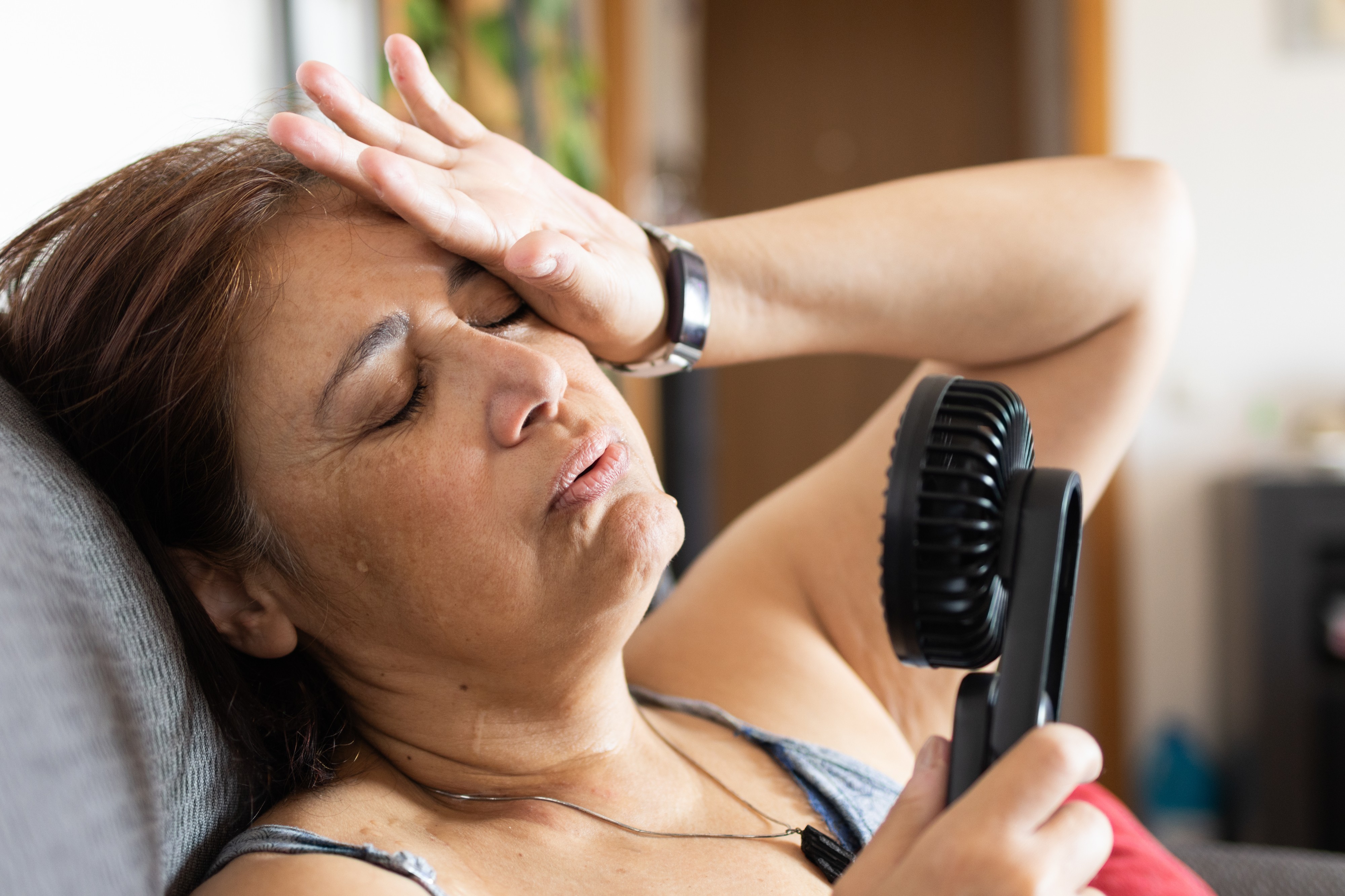 Woman looks tired holding a small fan