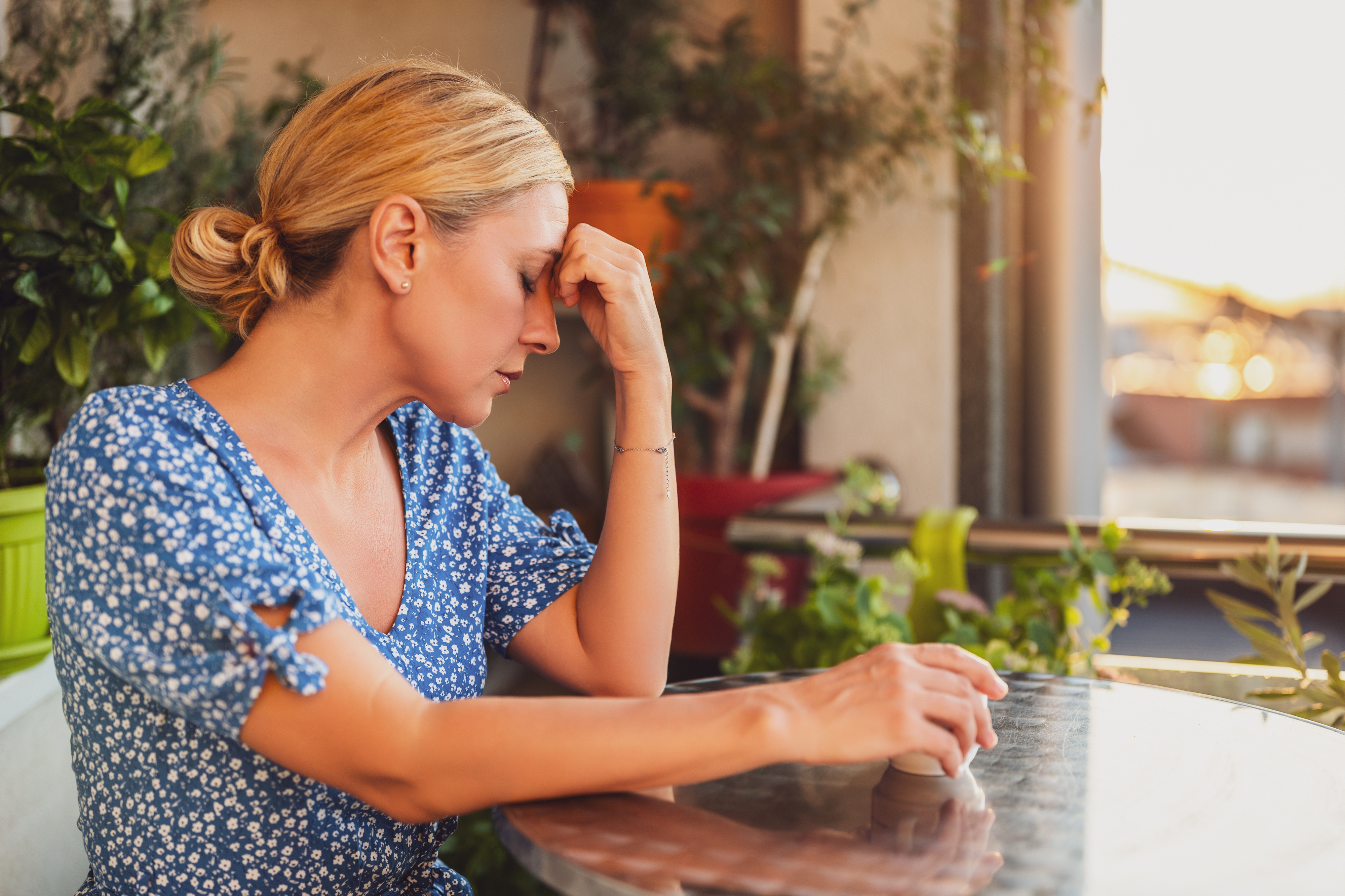 Woman at a table appears stressed or contemplative, surrounded by plants