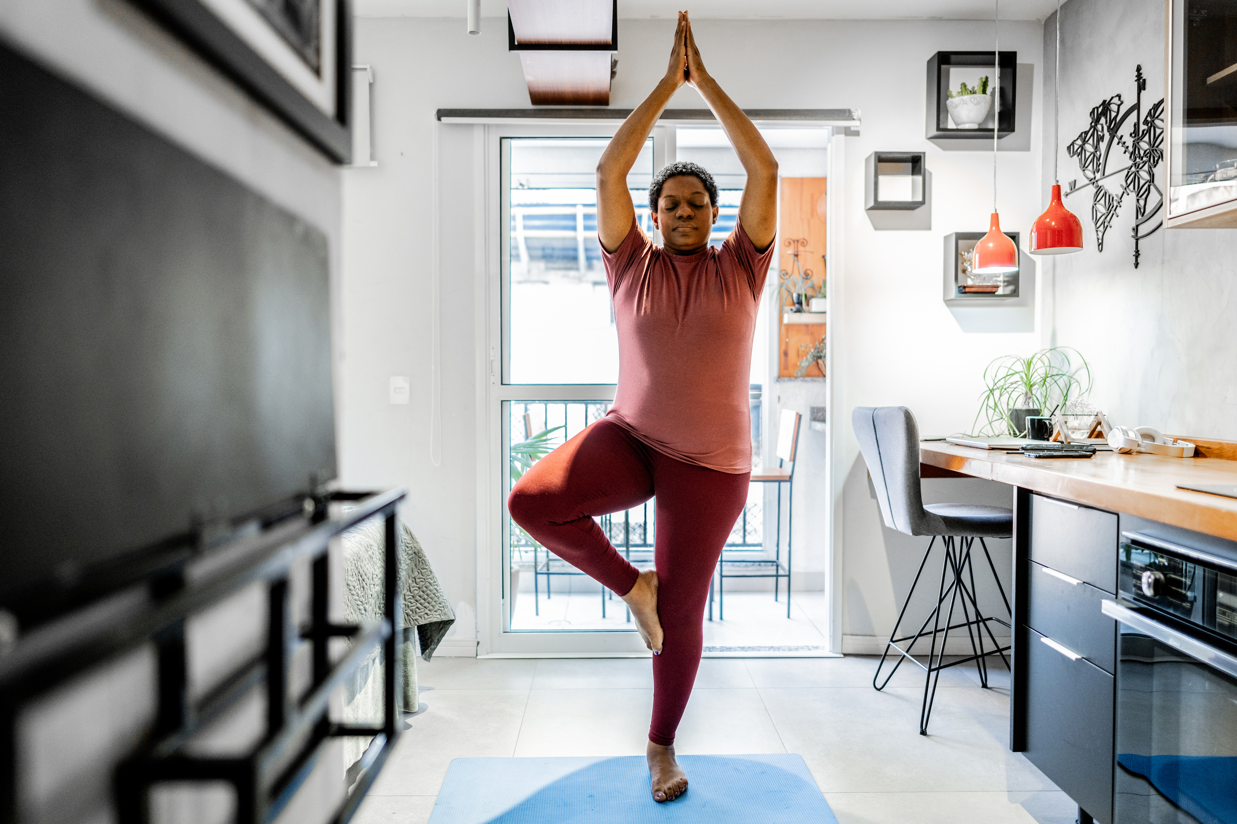 Woman practicing tree pose on a yoga mat in a home kitchen