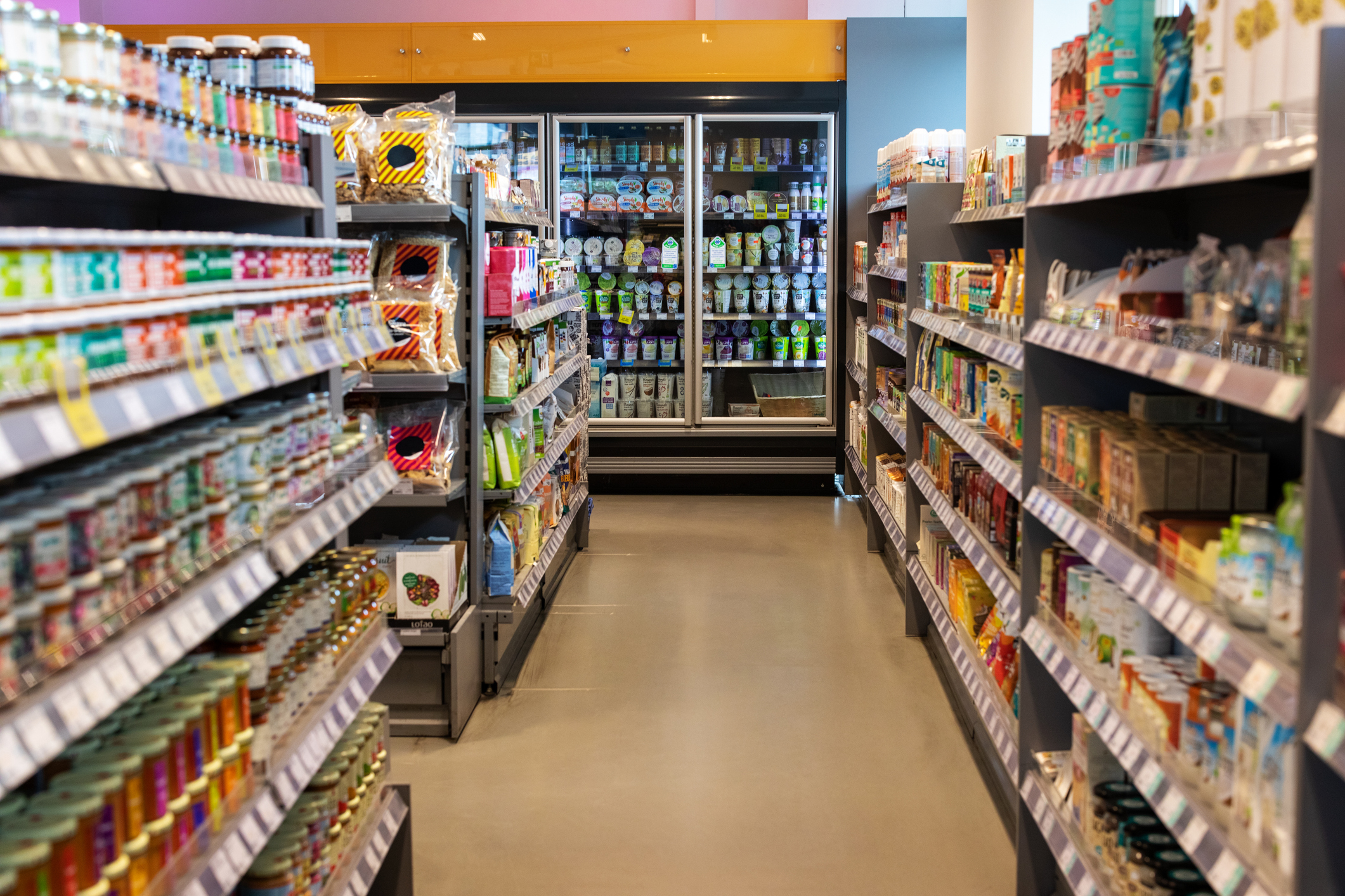 Grocery store aisle with various products on shelves leading to refrigerated section
