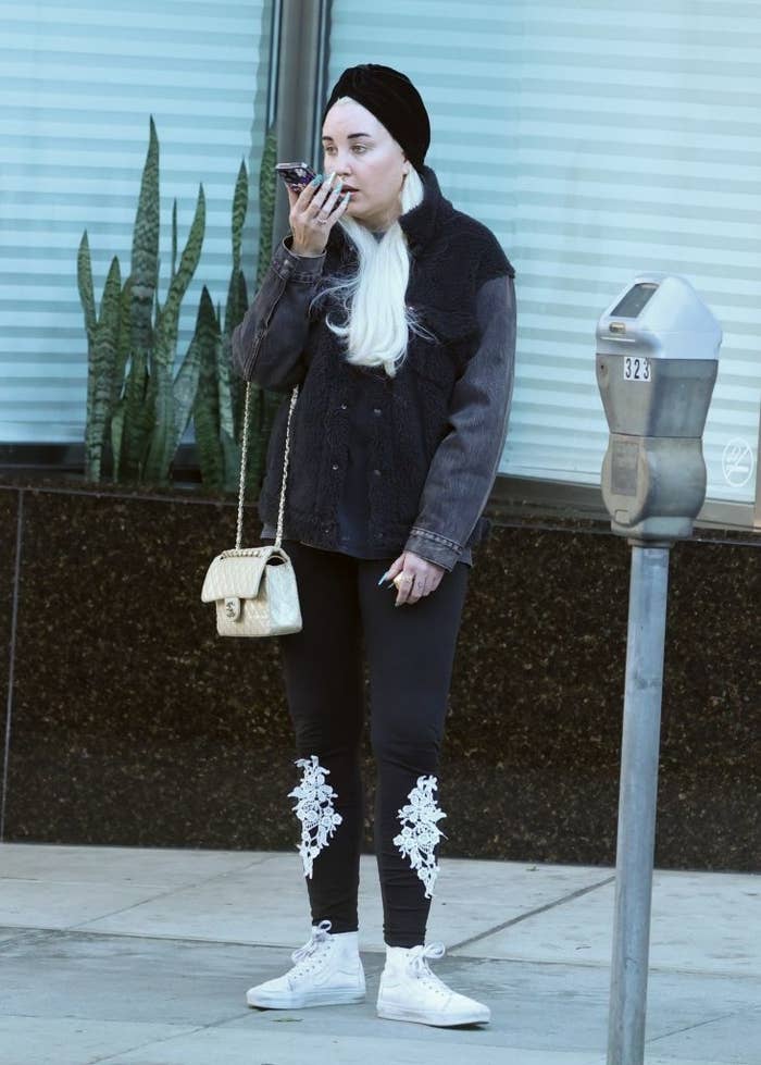 Amanda on street speaking on phone, wearing a jacket and turban, embellished pants, carrying a shoulder bag