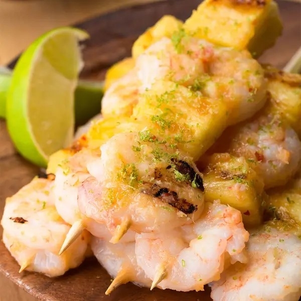 Grilled shrimp skewers with lime wedges on a wooden board