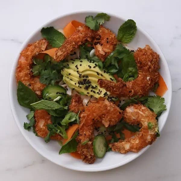 Plate with crispy shrimp, avocado, cucumber, herbs, and sesame seeds