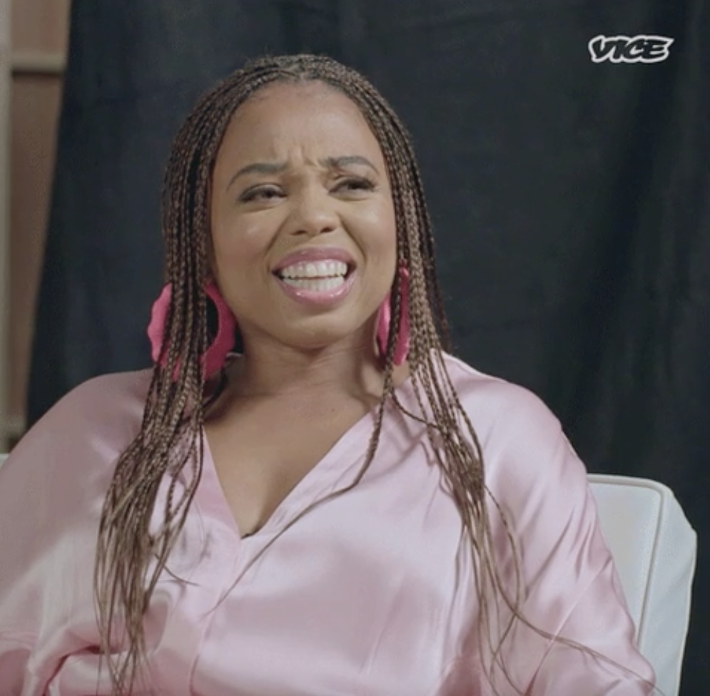 Jemele Hill with long braids wearing a blouse smiles with a slight grimace during an interview