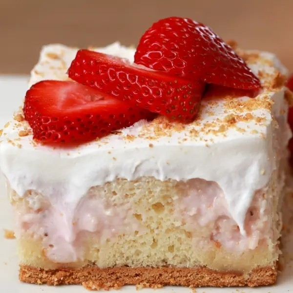A slice of strawberry shortcake with whipped cream topping and fresh strawberry slices