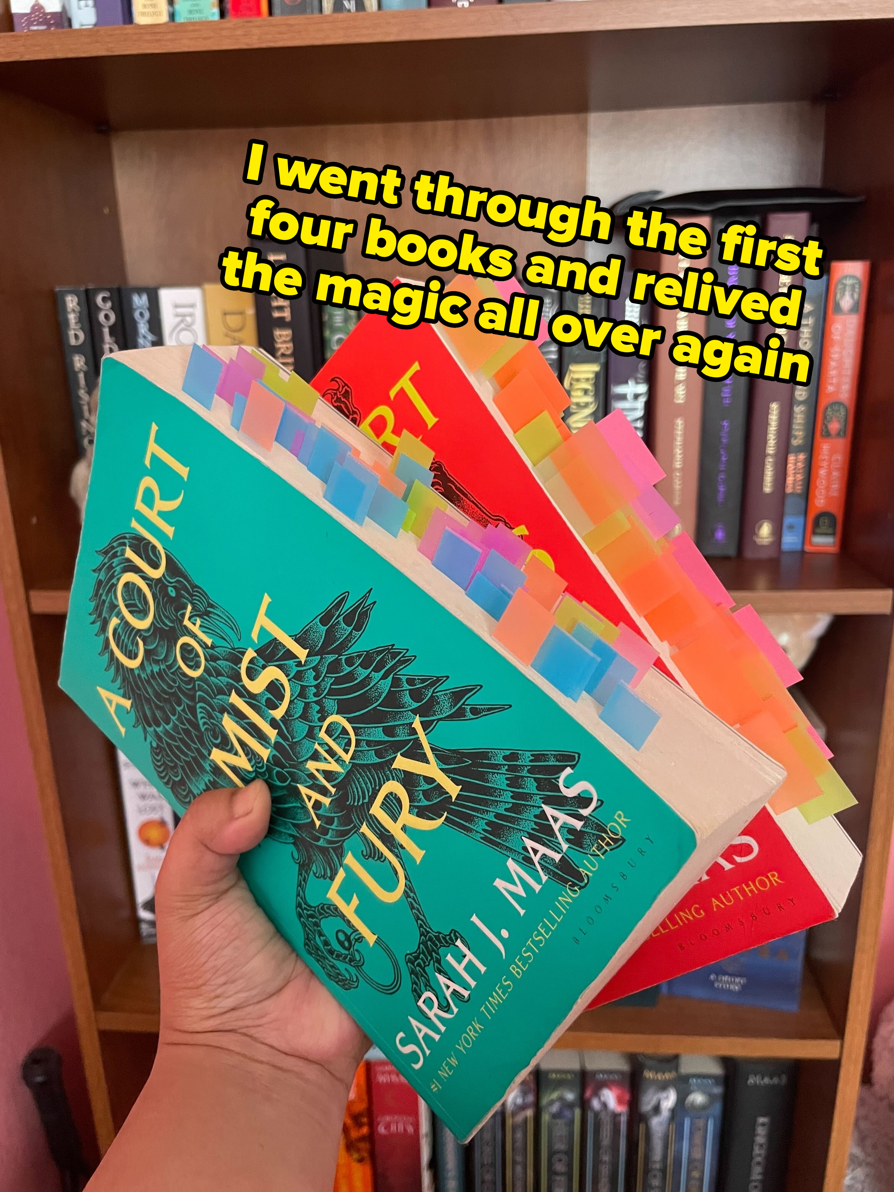 Hand holding "A Court of Mist and Fury" by Sarah J. Maas with bookshelf in background