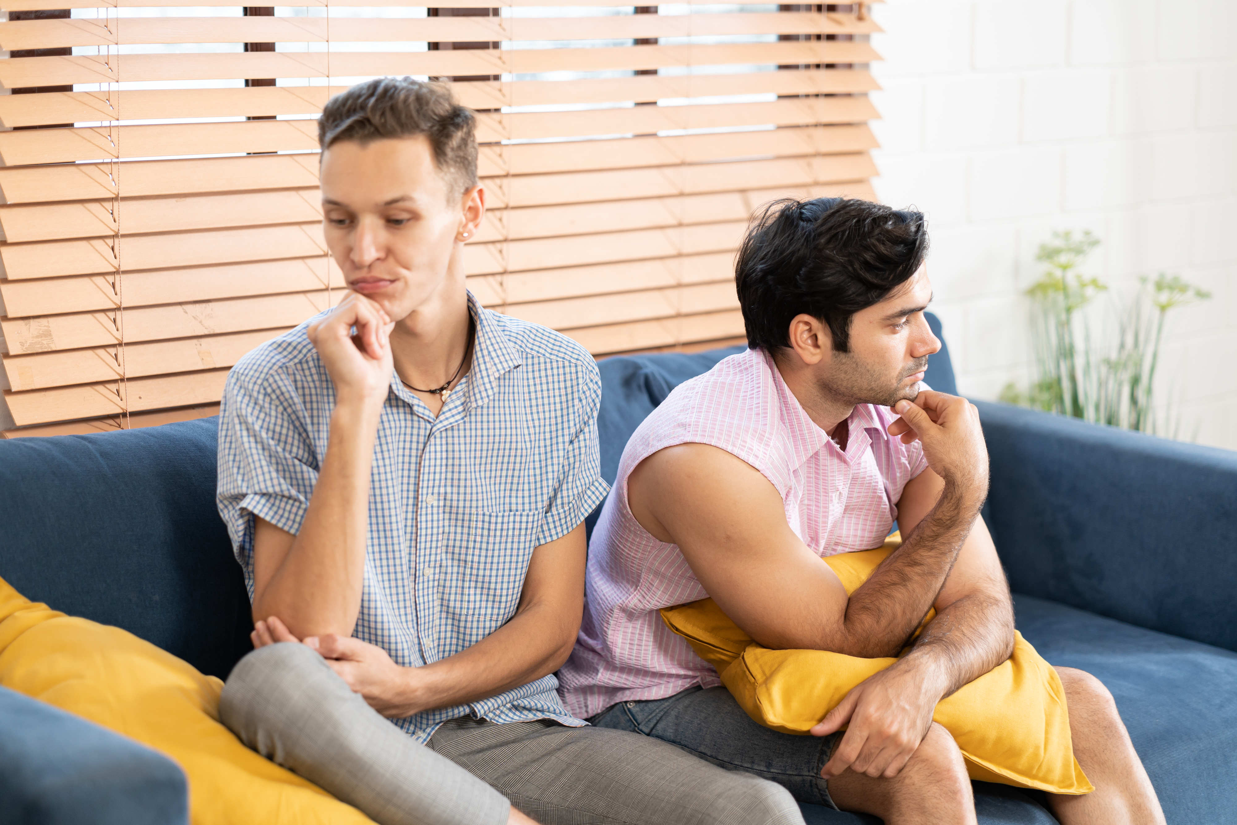 Two people sitting back-to-back on a sofa with contemplative expressions, possibly after an argument