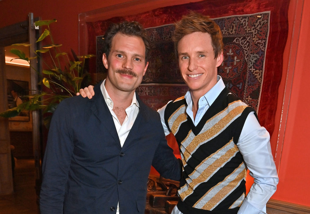 Two men posing together, one in a blue jacket and the other in a patterned sweater vest