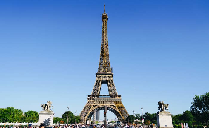 Eiffel Tower centered between two statues with clear skies, people visible at its base