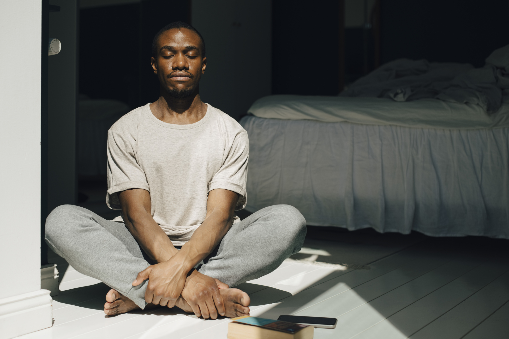 A person meditating on the floor next to a bed with a book beside them, promoting mindful parenting