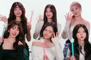 Six members of the music group IVE posing with light sticks, smiling and waving at the camera