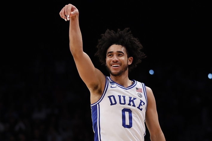 Basketball player in Duke jersey number 0 smiling and pointing upwards