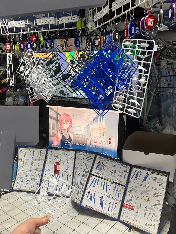 アニメキャラクターが描かれたモニターと、様々なキーホルダー、フィギュアパーツが展示された写真です。