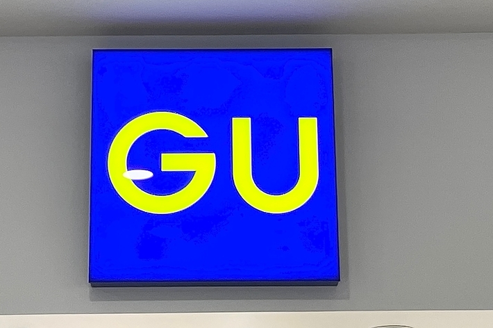 Sign with &ldquo;GU&rdquo; on a blue background, mounted on a wall above recessed lighting