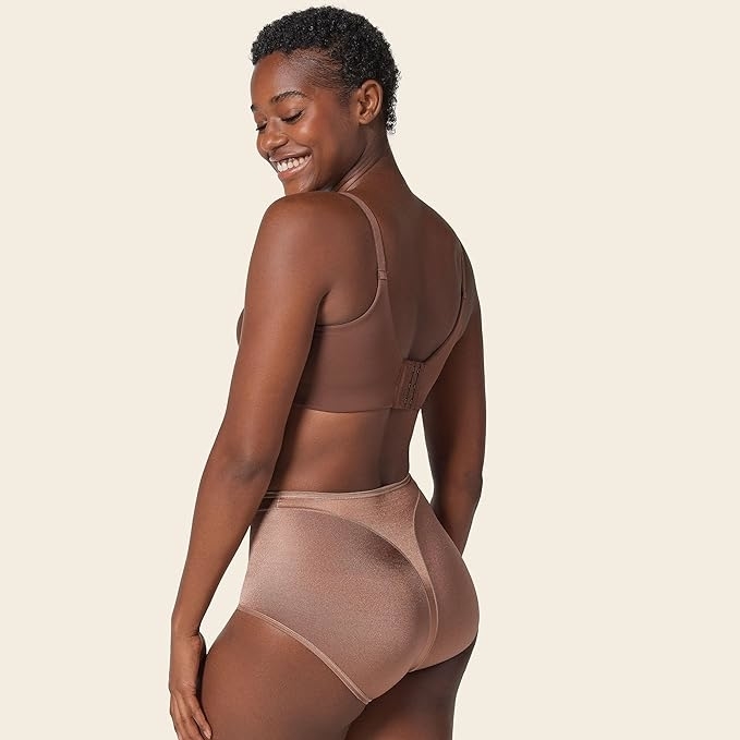 Model showcases high-waisted shapewear and supportive bra, smiling over her shoulder