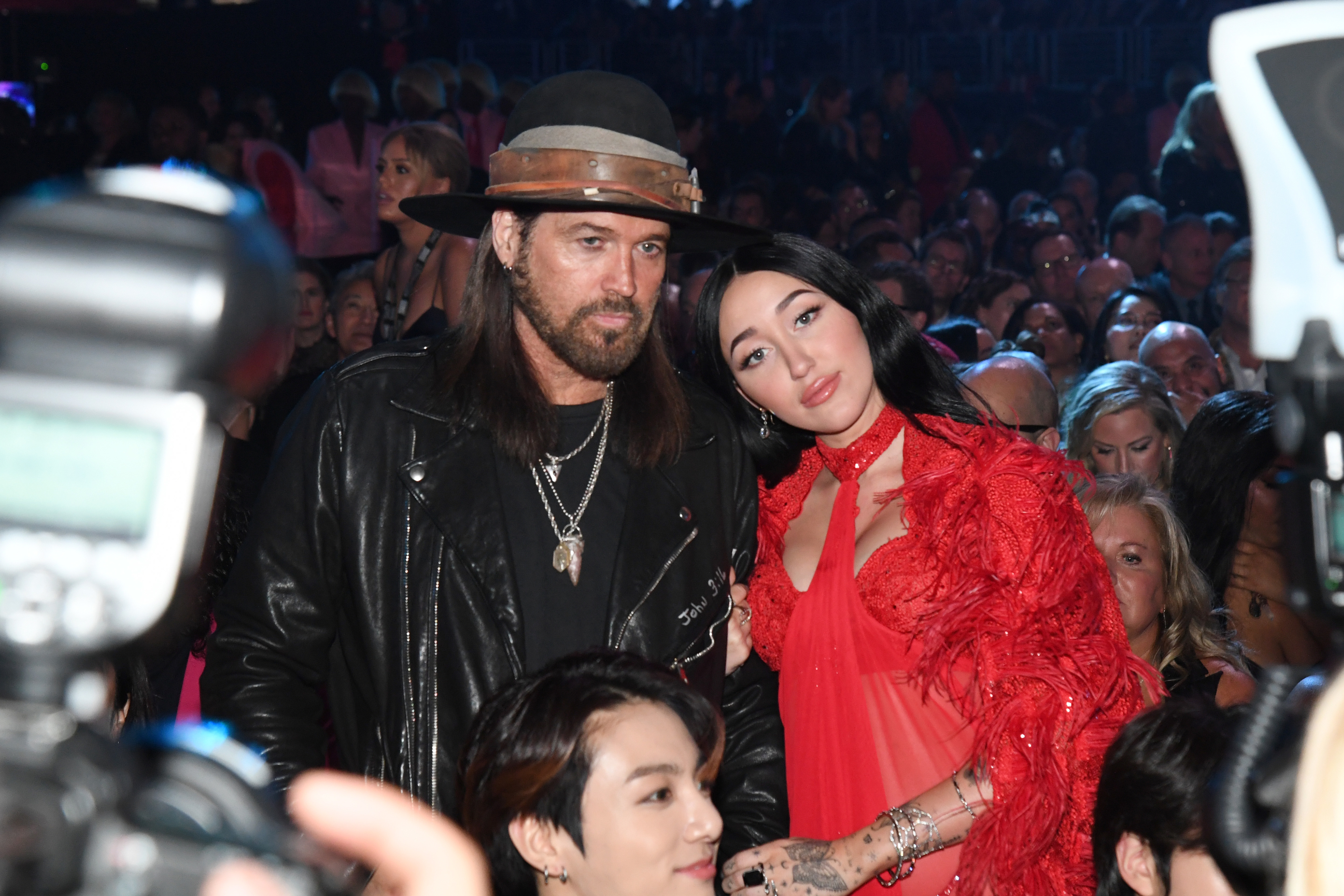 Billy Ray Cyrus and Noah Cyrus at an event, with Billy wearing a hat and leather jacket, Tish in a ruffled outfit