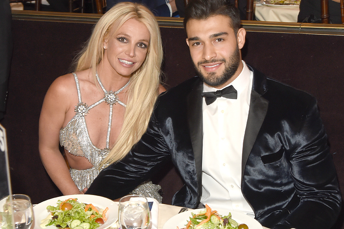 Britney Spears in a sparkling dress and Sam Asghari in a tuxedo sitting at a dinner table