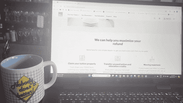 Laptop screen showing a tax services webpage, with a coffee mug in the foreground that has text