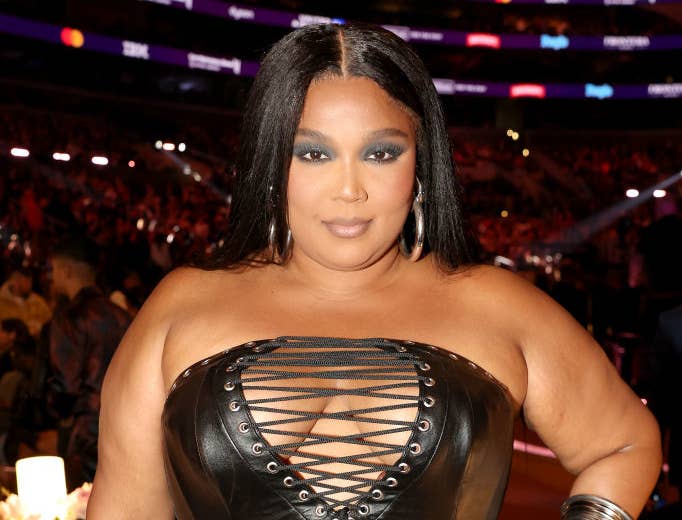 Lizzo at an event wearing a strapless leather dress with crisscross detailing on the bodice, accessorized with bangle bracelets