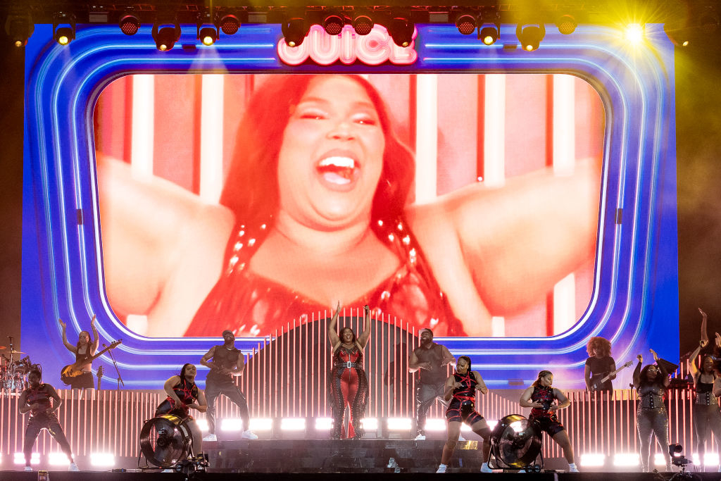 Lizzo performs onstage with dancers and a giant screen displaying her image during a concert