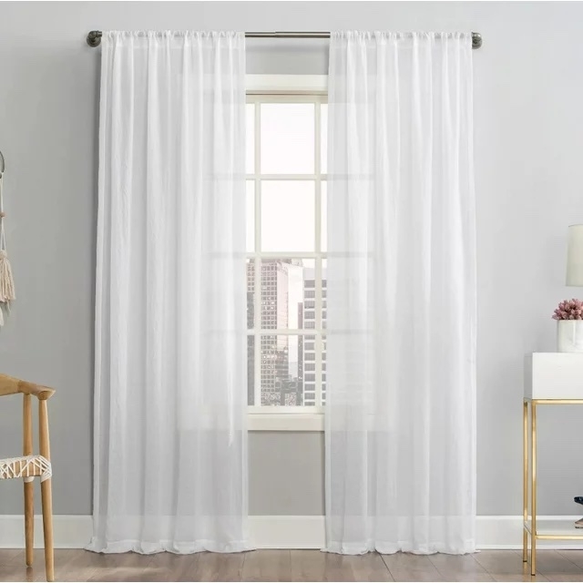Sheer white curtains hang in front of a window in a well-lit room