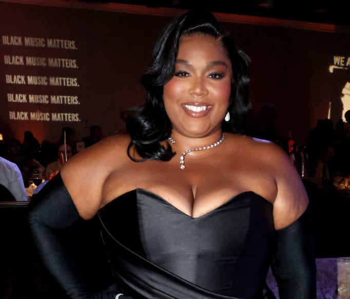 Lizzo in a black off-the-shoulder dress with pearl necklace and gloves, at an event
