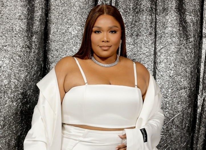 Lizzo poses in a white, off-the-shoulder outfit with ruffles, accessorized with a choker