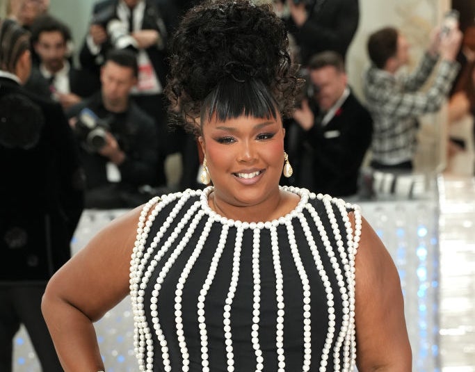 Lizzo in a black dress with pearl-like embellishments, posing on the red carpet