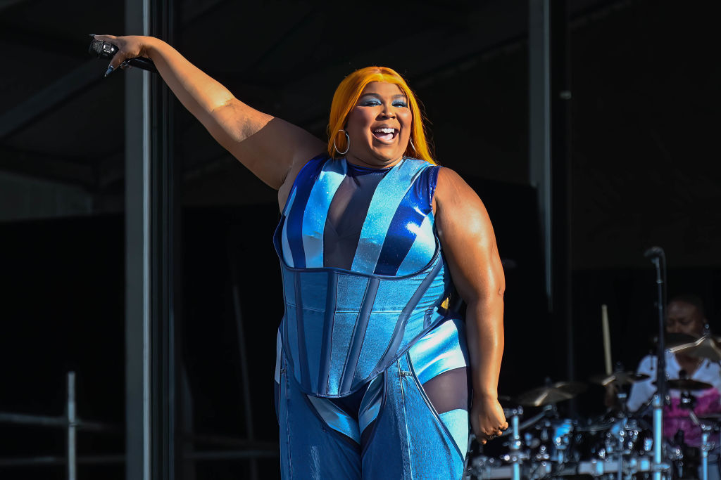 Lizzo performs onstage in a sleeveless striped outfit, engaging with the audience