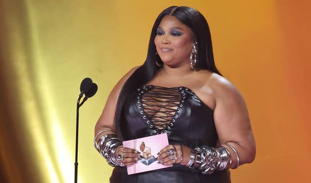 Lizzo in a black laced-up outfit with statement jewelry stands at a podium on stage