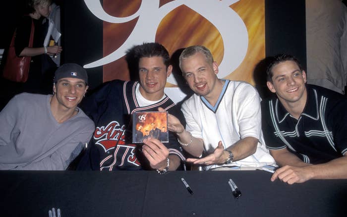 The members of 98 Degrees sitting at a signing table with their CD