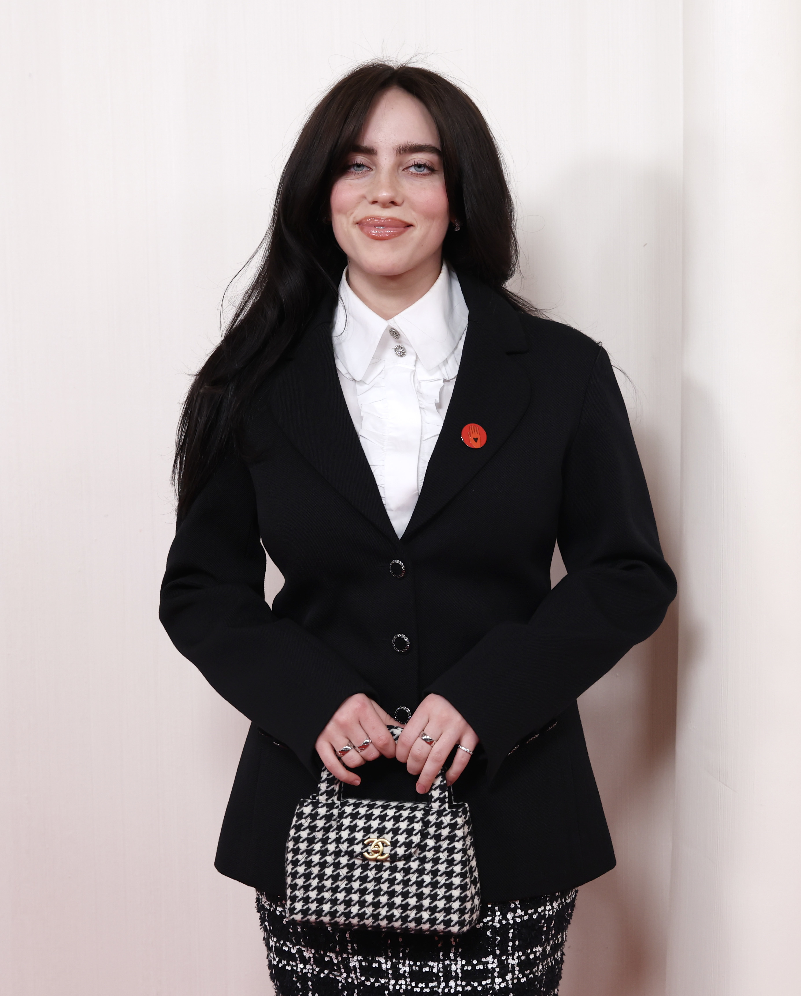 Billie Eilish in a blazer, shirt, holding a checkered handbag