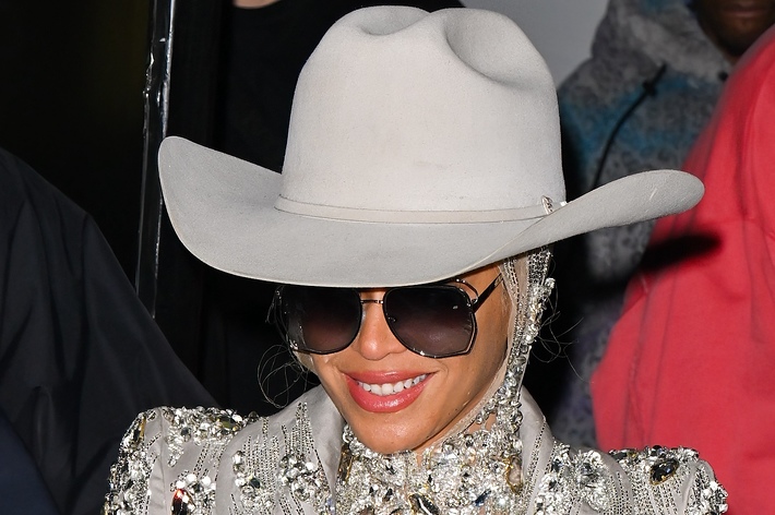 Person in ornate outfit with wide-brimmed hat and sunglasses, smiling
