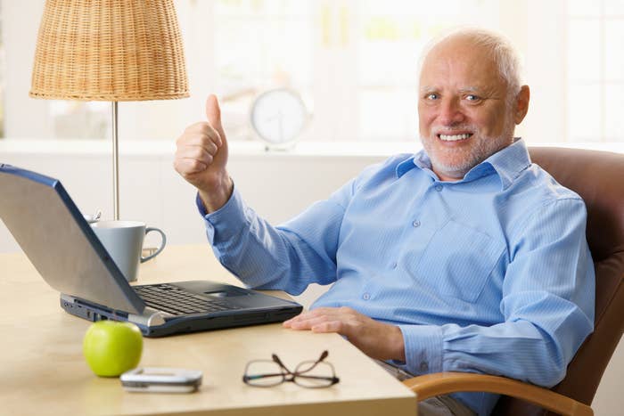 Man sitting at a desk with a laptop gives a thumbs up
