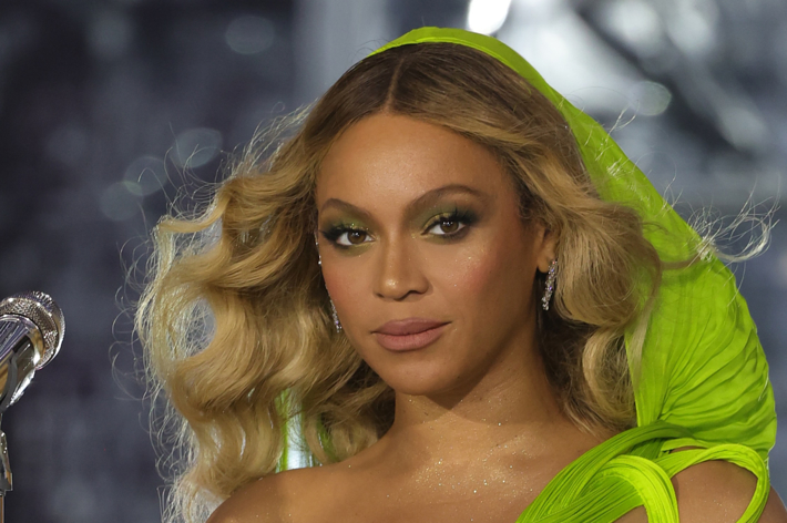 Beyoncé wearing a green outfit with sheer sleeves, standing at a microphone