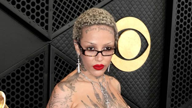 Person with short hair and large earrings stands in front of Grammy Awards backdrop